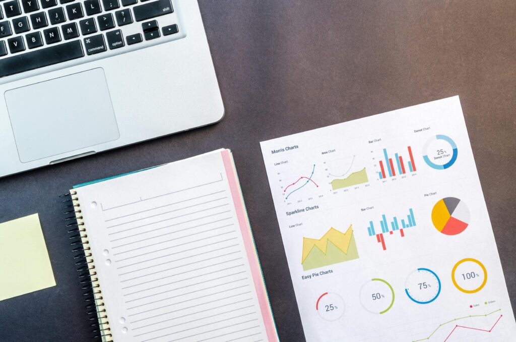 Top view of a laptop, notebook, and data charts on a table, ideal for business and work themes.